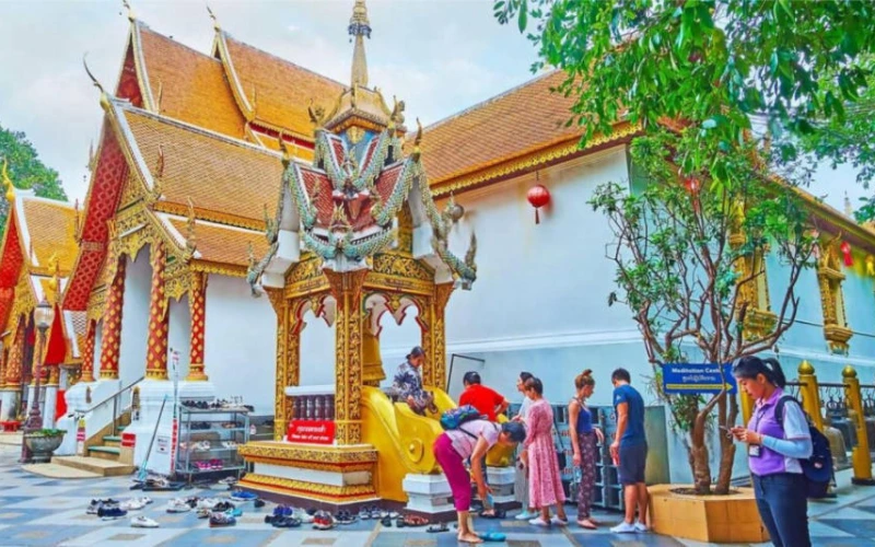 Fila de visitantes no pavilhão Mondop ornamentado, com sino ritual, no Wat Doi Suthep